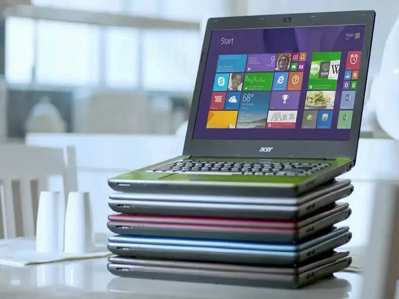 Stack of colorful laptops with one open laptop displaying Windows interface on top