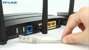 Hand connecting an Ethernet cable to a Wi-Fi router or modem during internet setup and network installation service.
